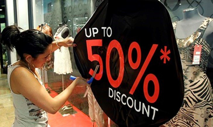 A woman sticks a discount sign on a shop window